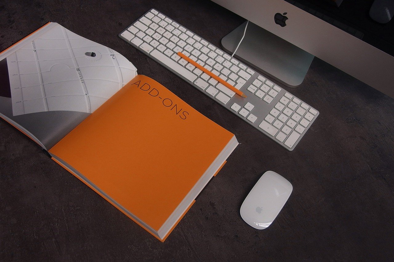 Otwarty notatnik, biała klawiatura i mysz komputerowa leżące na biurku